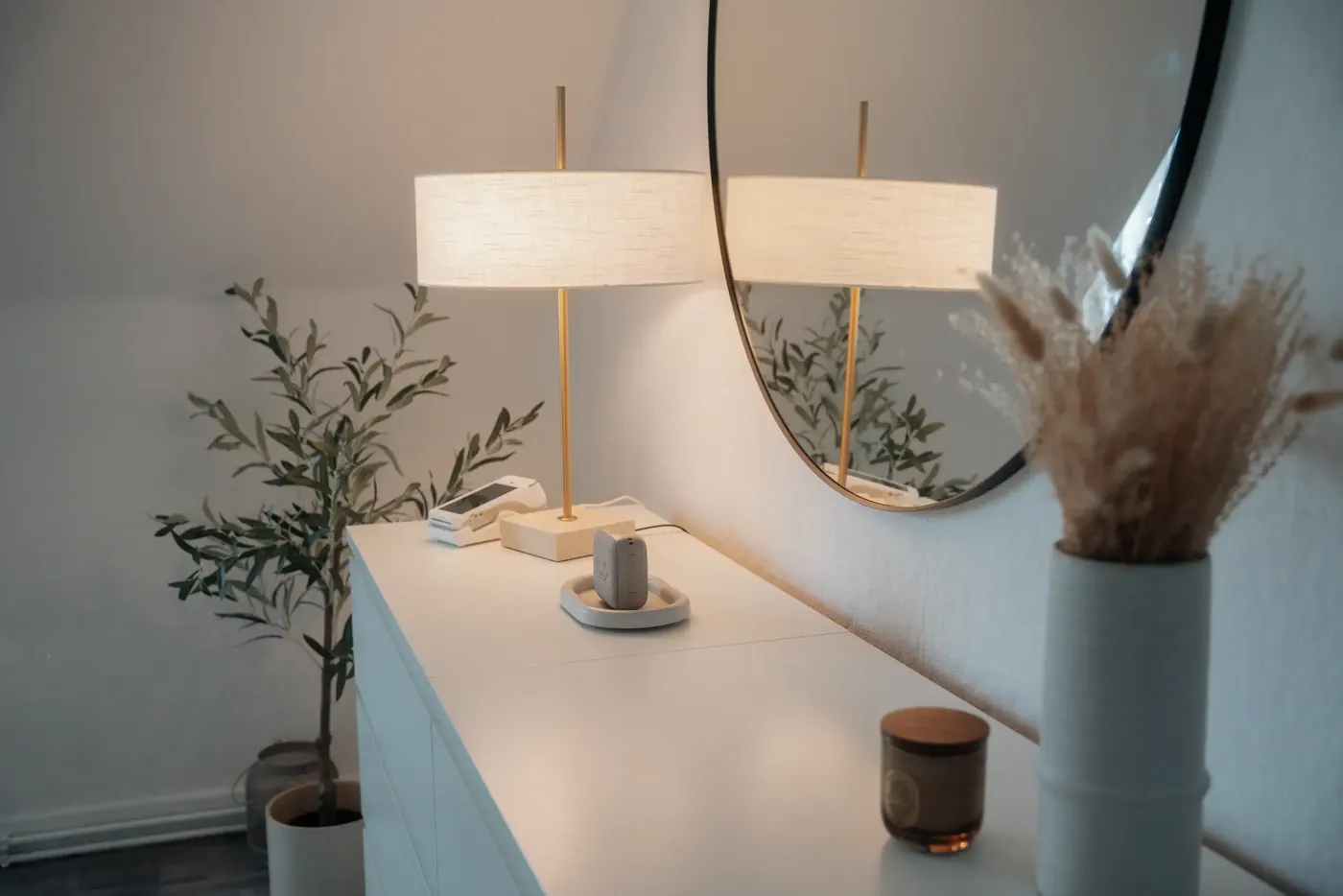 Weiße Kommode mit Tischlampe, Olivenbaum und rundem Spiegel im Studio