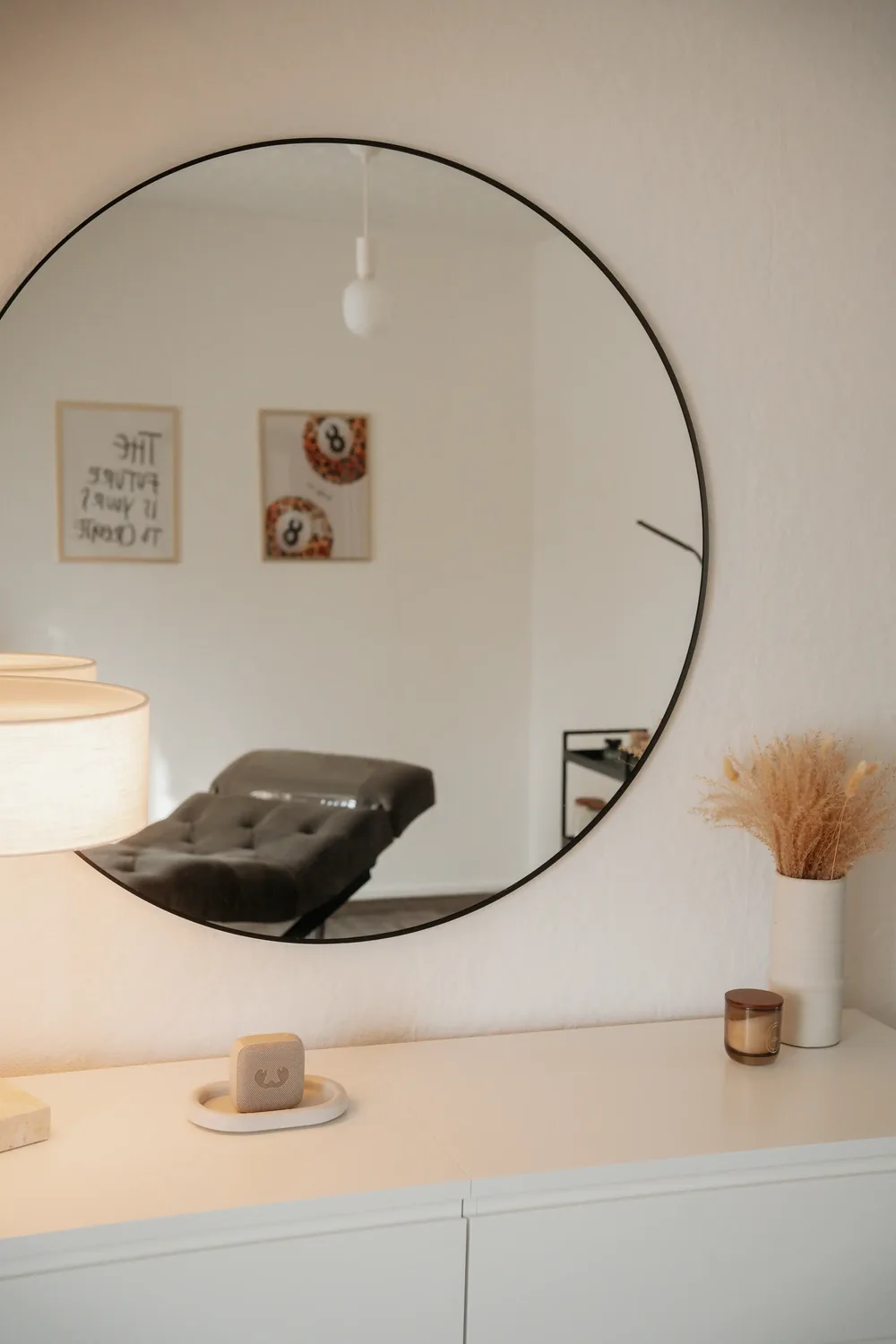 Runder Wandspiegel über einer weißen Kommode, im Spiegel eine Behandlungsliege
