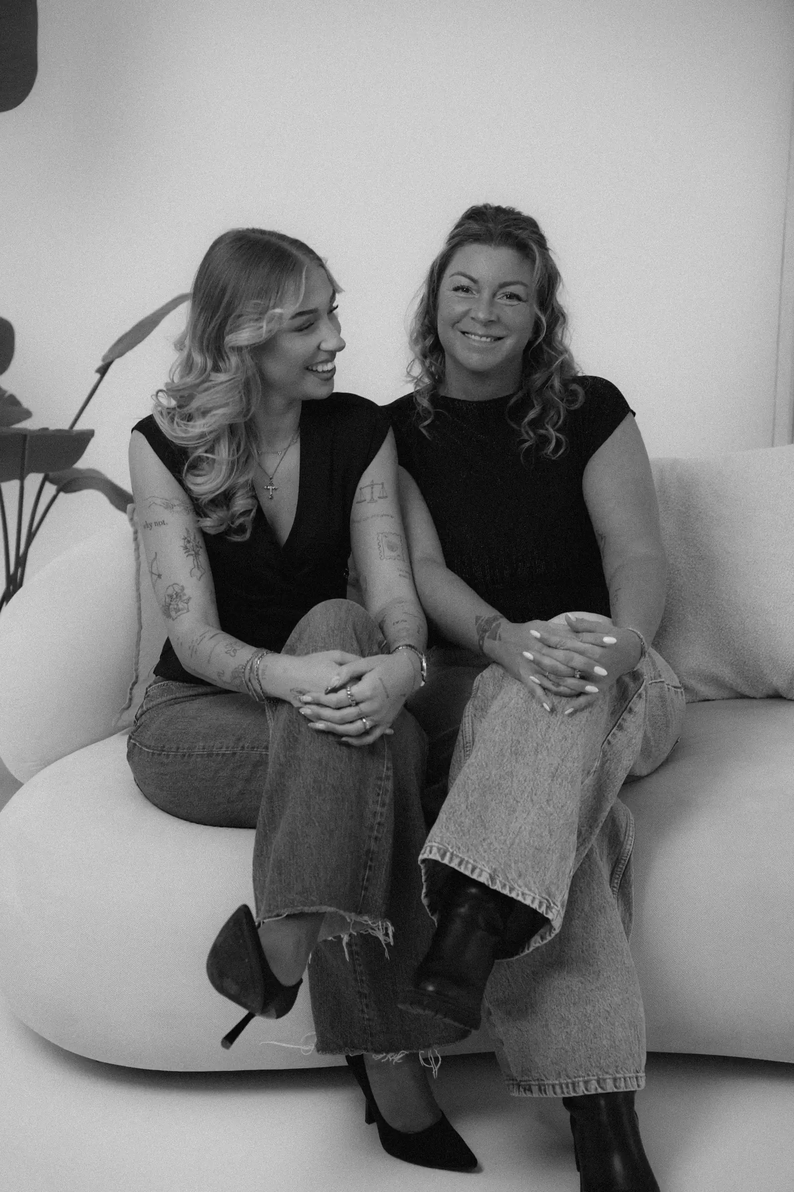 Diana und Jasmin sitzen lachend nebeneinander auf einem hellen Sofa, Schwarz-Weiß-Aufnahme