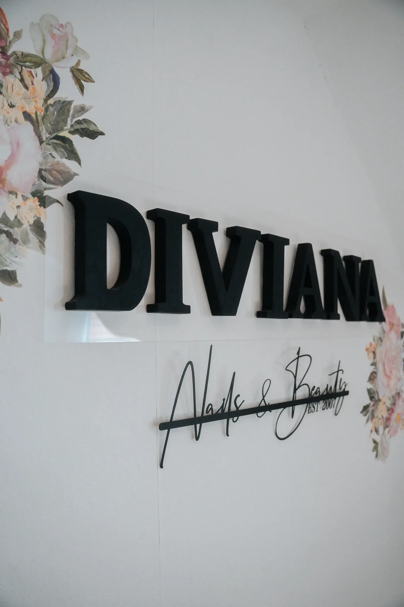Der Diviana-Schriftzug „Nails & Beauty“ an der Studiowand, umrahmt von Blumenmotiven