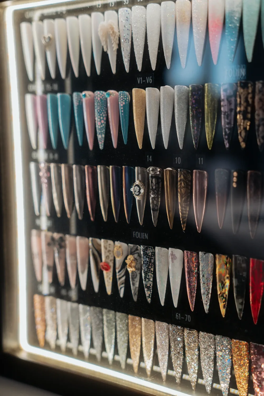 Beleuchtete Tafel mit vielen Nail-Art-Designs in verschiedenen Farben und Mustern